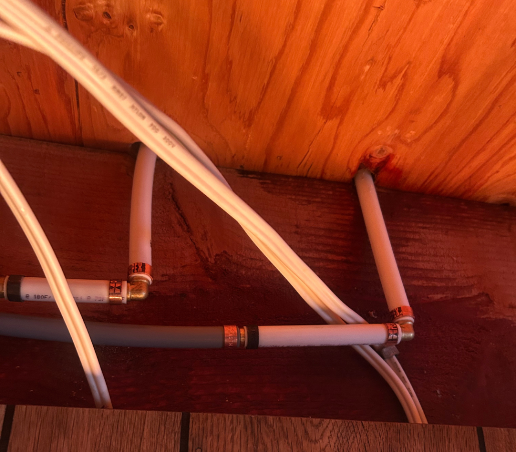What Happens During Poly-B Replacement? A Homeowner’s Guide 2 Grey Poly-B pipe running horizontally below newer white PEX plumbing installed between wood floor joists.